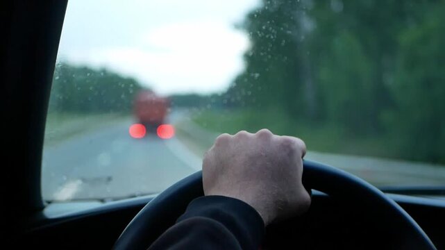 A close-up of a person's hand on the steering wheel while driving on a rainy road. Video for topics to transportation, travel, driving, trips, automobiles, safety, or navigation