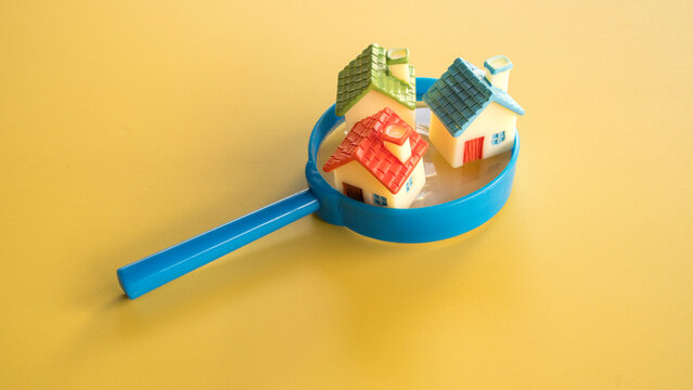 Three colorful miniature model houses with red green and blue roofs sitting inside the rim of a blue magnifying glass on yellow.