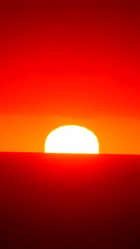 Sunset, sun, horizon, glowing golden sphere disappearing below the deep orange skyline, beautiful natural phenomenon creating a tranquil and atmospheric background for creative projects