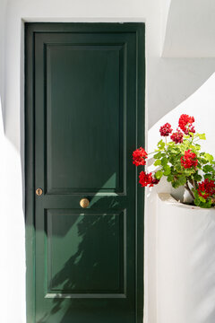 Green door with red geraniums on white Mediterranean wall, Italy