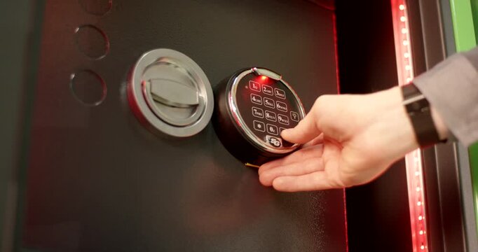 Person opening a safe door with a numeric keypad to retrieve a small item from a plastic drawer