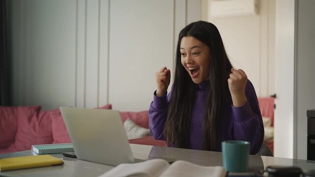 Young Asian woman reading a good news email on laptop, celebrating a grant award