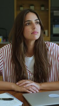 Thoughtful young woman sitting at her desk, looking away with a pensive expression, considering ideas and solutions while working or studying from home in a modern apartment interior