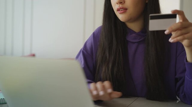 Young Korean woman shopping online on a laptop, entering credit card information