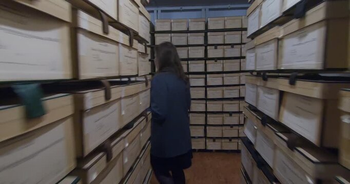 Document storage area. An archivist walks between rows of shelving units filled with folders and boxes.