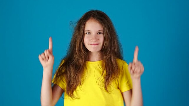 Cute european smiling girl holding hands and index fingers up against blue background