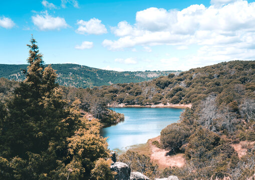 Vista panor&aacute;mica de un lago azul rodeado de colinas boscosas bajo un cielo nublado