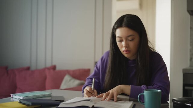 Tired Korean woman studying at home, writing an essay under academic pressure