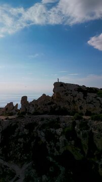 Dingli Cliffs Malta aerial drone view of a person standing on edge of steep rocky cliff.
