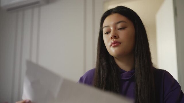 Young Korean woman opening an envelope and reading a letter at home