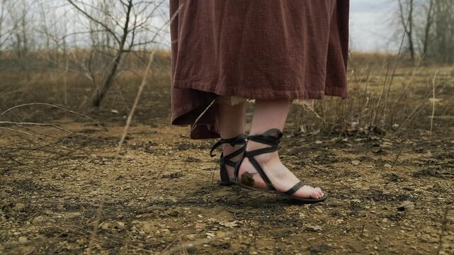 Ancient Journey: A close-up shot focuses on a woman's feet adorned with gladiators' sandals as she walks on arid, dry land, hinting at a journey through rugged terrain.