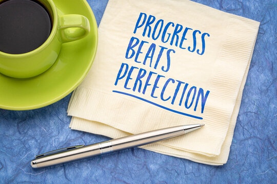 Progress Beats Perfection &ndash; inspirational handwritten note on a napkin with coffee and pen, encouraging consistent improvement over perfectionism.