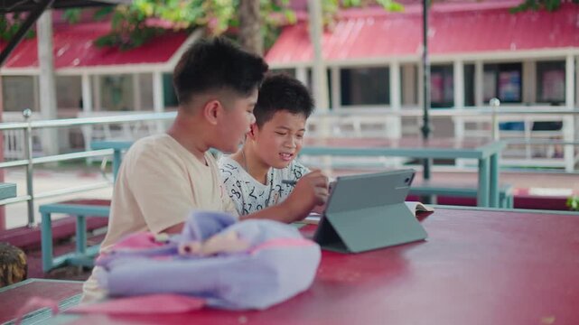 Group of smart Asian schoolboys tutoring homework and helping each other understand the academic lesson. Happy primary students studying with textbooks together.
