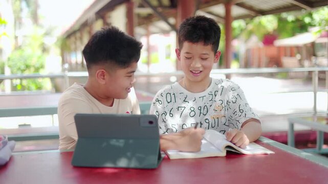Group of smart Asian schoolboys tutoring homework and helping each other understand the academic lesson. Happy primary students studying with textbooks together.