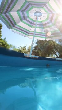 Vertical view of a parasol beside a private above ground swimming pool in a garden with a relaxing summer outdoor atmosphere