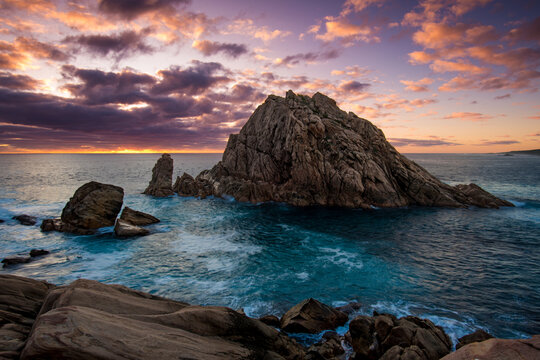 View of Sugarloaf Rock surrounded by crashing ocean waves under a dramatic sunset sky with vibrant clouds in Dunsborough, Western Australia, Australia.