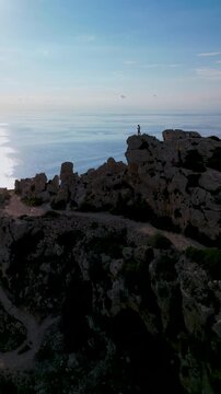 Dingli Cliffs Malta aerial drone view of a person standing on edge of steep rocky cliff.
