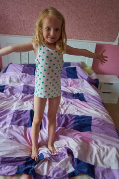 Happy little child playing on unmade bed, Cute little blonde girl in star pattern pajamas jumping on bed in a cozy bedroom