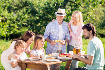 Fototapeta premium Multi-generation family enjoying an outdoor picnic together in a sunny garden with grandparents serving pastries and everyone smiling and sharing food