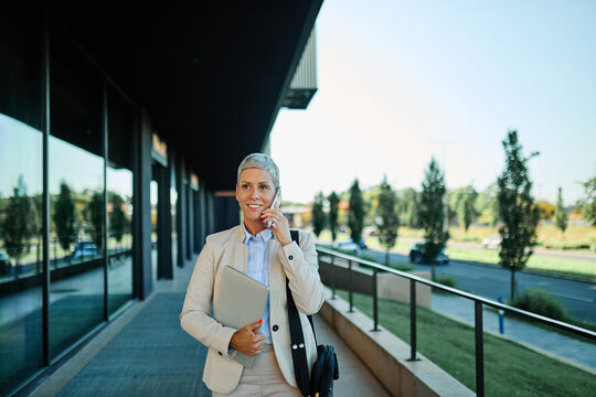 Portrait of a young  businesswoman woman using a smartphone mobile phone walking down the street, surrounded by moder corporate office buildings