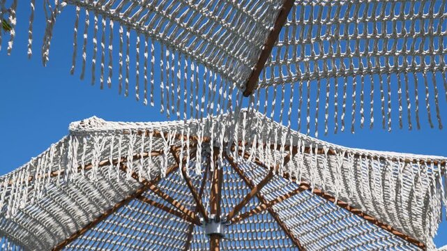 White Woven Cotton Macrame Beach Parasol with Decorative Fringe and Wooden Ribs Under Clear Summer Sky, Tropical Paradise Vacation and Luxury Leisure Background