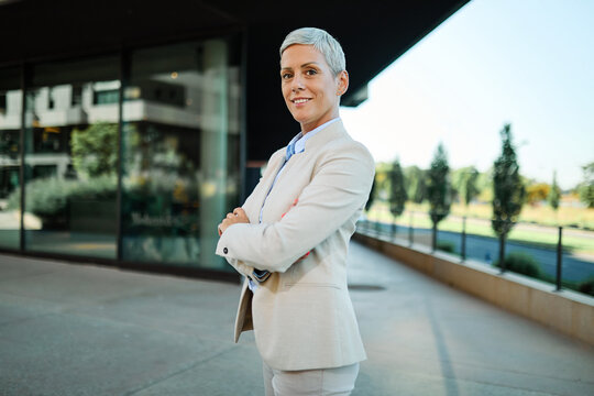 Portrait of a young  businesswoman woman walking down the street, posing and looking at camera, surrounded by moder corporate office buildings