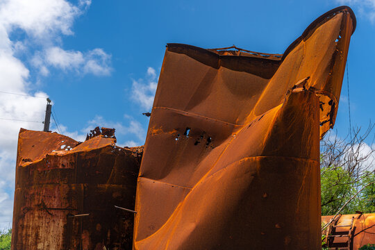 View of rusted and damaged industrial metal tanks standing against a bright blue sky in San Jose, Tinian, Northern Mariana Islands.