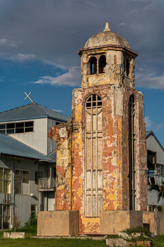 View of the historic ruins of the San Jose Catholic Church bell tower with weathered orange and yellow plaster walls against a blue sky in San Jose, Tinian, Northern Mariana Islands.