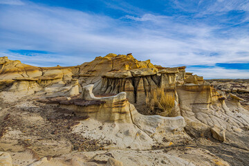 Weathered sandstone formations with sparse desert vegetation in Bisti Badlands, New Mexico. Blue sky over unique geological landscape. © ZL Visuals