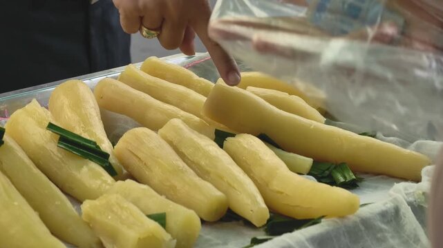 Close-up with rack focus of hands choosing steamed cassava at a street food market