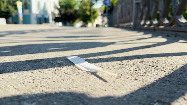 A white feather lies silently on a sunny sidewalk under fence shadows in Simferopol, Crimea. The lonely scene brings a peaceful and serene feeling.