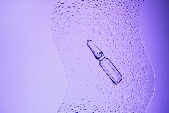Glass ampoule containing liquid on textured surface with water droplets and copy space