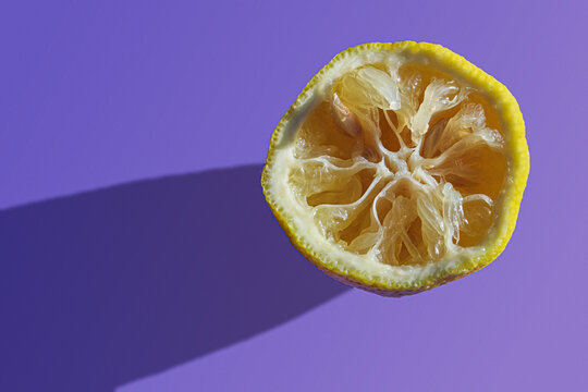 Squeezed lemon half showing dryness and lack of juice on vibrant purple background