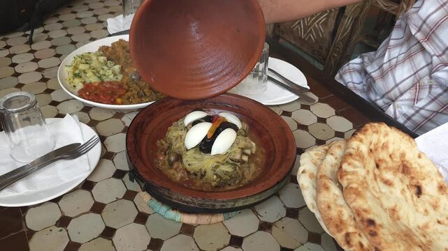 Traditional Moroccan tagine with meat, vegetables, onions, olives, and spices served in a clay tagine dish. Freshly cooked authentic North African meal steaming hot on a rustic table.