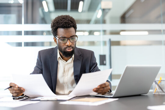 Adult male professional working diligently at a desk, reviewing important documents and utilizing a laptop for business analysis in a corporate environment