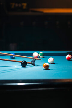 Billiard Game in Action: A close-up of a blue billiard table with various colored balls scattered, a cue stick poised to strike the black ball.