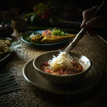 Authentic Bruneian Ambuyat set Hand using a candas to twirl sticky sago starch from a bowl, showcasing unique Southeast Asian dining