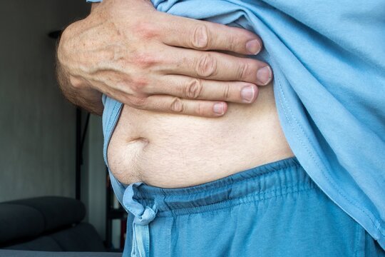 A middle-aged man holding his right hip with his left hand, representing right hip joint or muscle pain, injury, and medical symptoms of disease, side view.