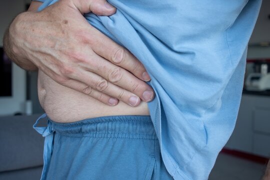 A middle-aged man holding his right hip with his left hand, representing right hip joint or muscle pain, injury, and medical symptoms of disease, side view.