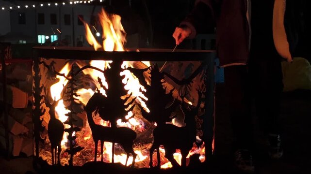 Fire Pit with Decorative Wildlife Cutouts and Person Tending the Flames at Night. 