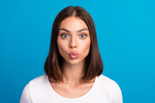 young woman with brunette bob makes a playful kissy face against a bright blue background wearing a white shirt suitable for fashion lifestyle advertising