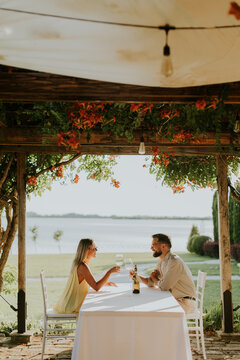 Couple enjoying drinks at a table near water during golden hour