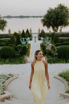 Woman walks down stone steps at garden near water during evening time