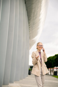 Woman talking on a phone near modern building with unique design in daytime