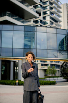 Business woman checks phone in front of modern building during the day