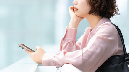 スマートフォンを持って考える女性・ビジネスウーマン, Businesswoman Thinking While Holding a Smartphone © Trickster*