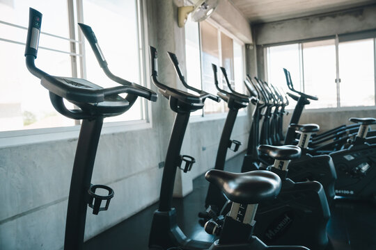 Exercise bike gym fitness cardio equipment indoor bicycle workout training health Exercise bike row inside bright indoor gym beside window, modern cardio equipment for workout, training, health