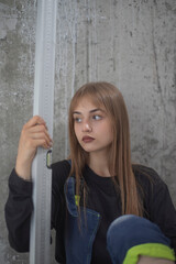Fototapeta premium Tired female builder holding spirit level tool sitting by concrete wall with copy space