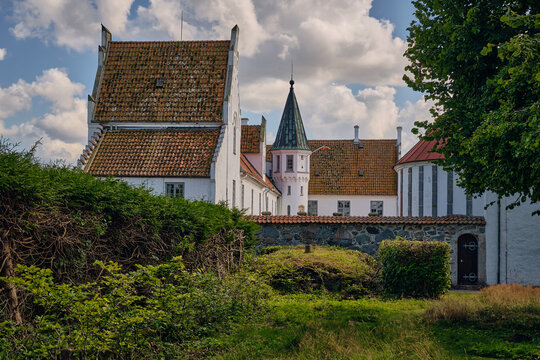 View of the historic Bosjokloster Abbey complex featuring white walls, terracotta tiled roofs, and a stone wall in the foreground, Bosjokloster, Skane County, Sweden.