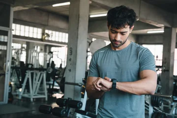 Man gym watch fitness exercise athlete checking wearable device in industrial training center with dumbbell equipment focused expression © chokniti